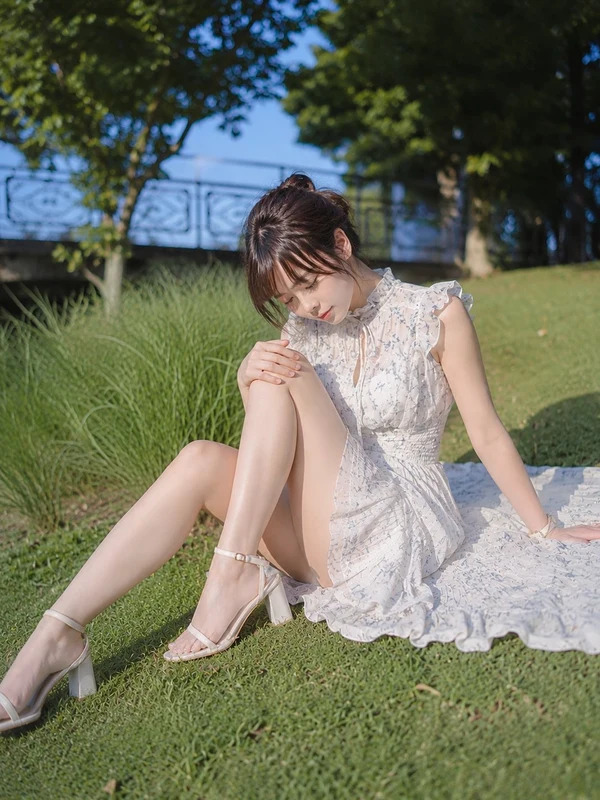 Woman in a pale floral dress seated in a sunlit park
